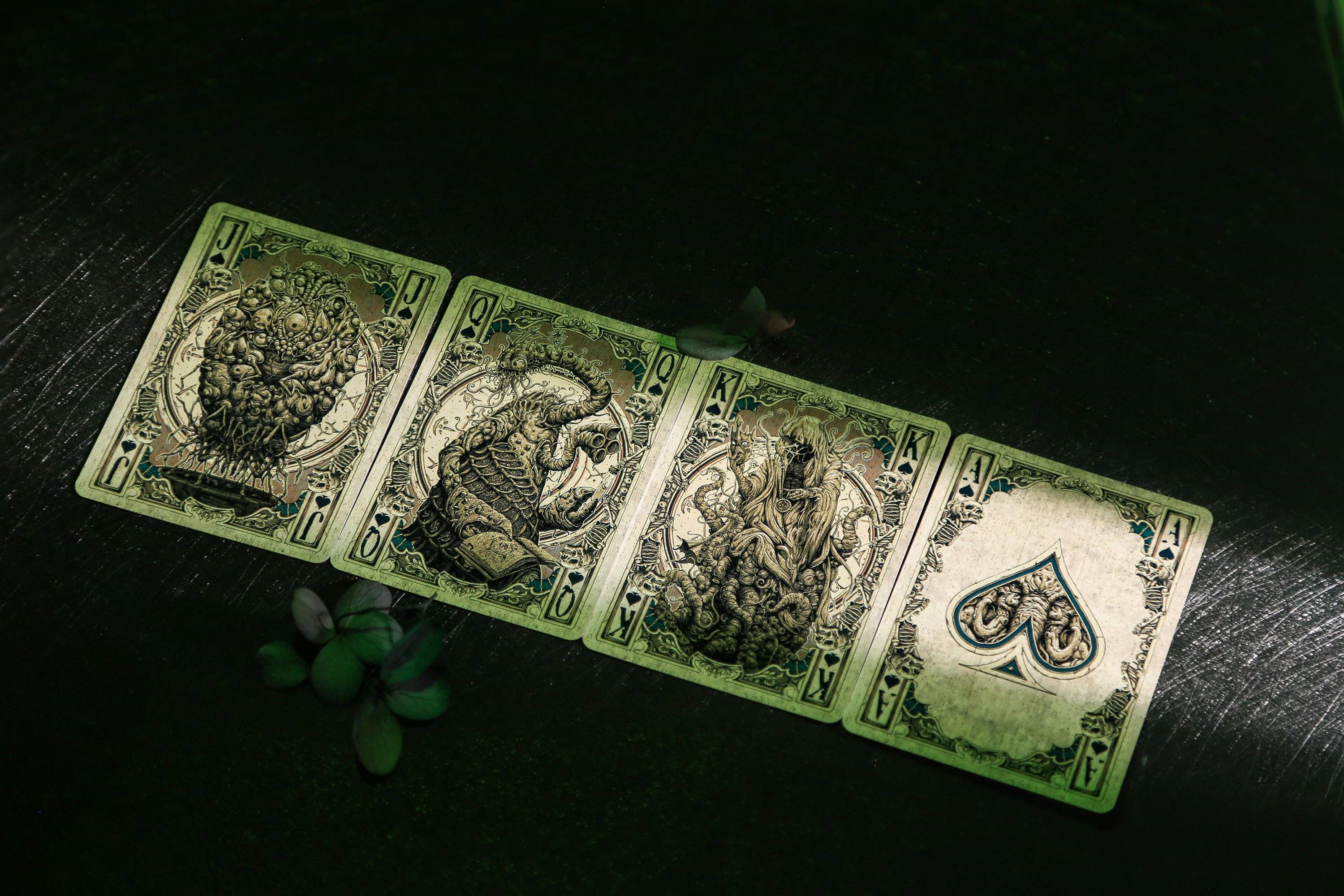 Four playing cards with green and black design on a dark surface