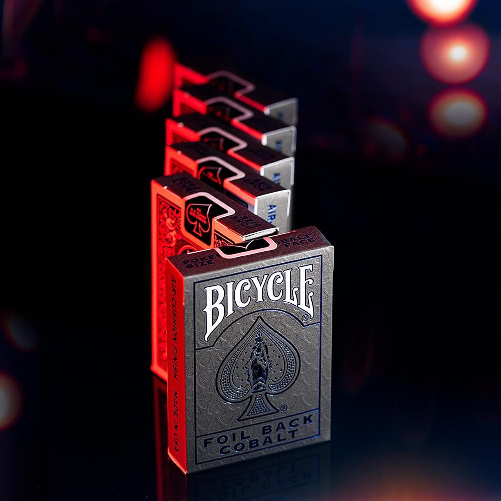 Row of Bicycle Foil Back decks with Cobalt box in front glowing under red and blue lights.