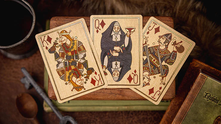 Three playing cards featuring different characters on a wooden surface with a book and other objects.