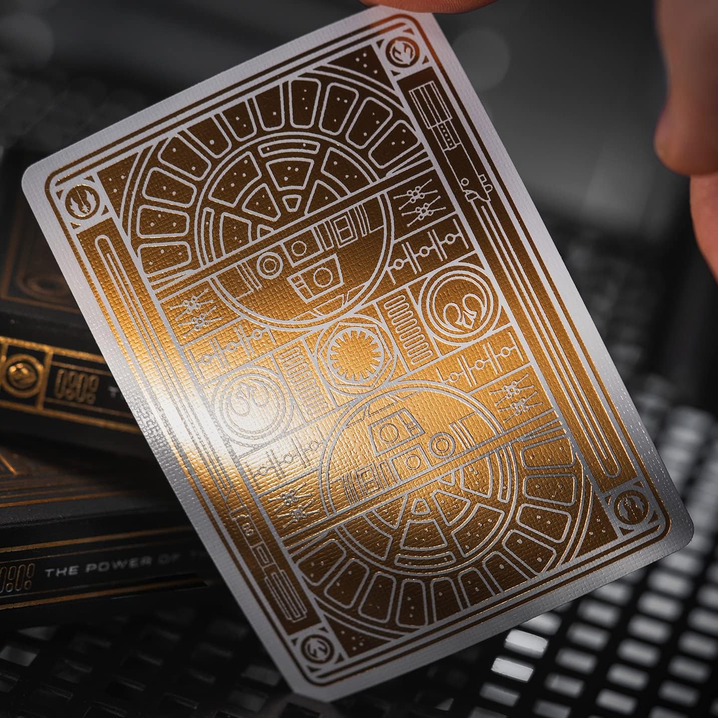 Gold playing card with intricate design held by a hand against a dark background