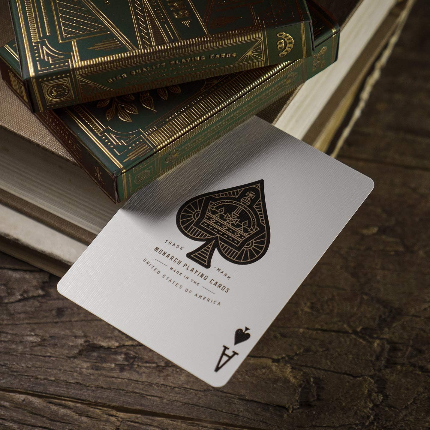Green Monarch playing card with spade symbol on a wooden surface with a deck of cards in the background.