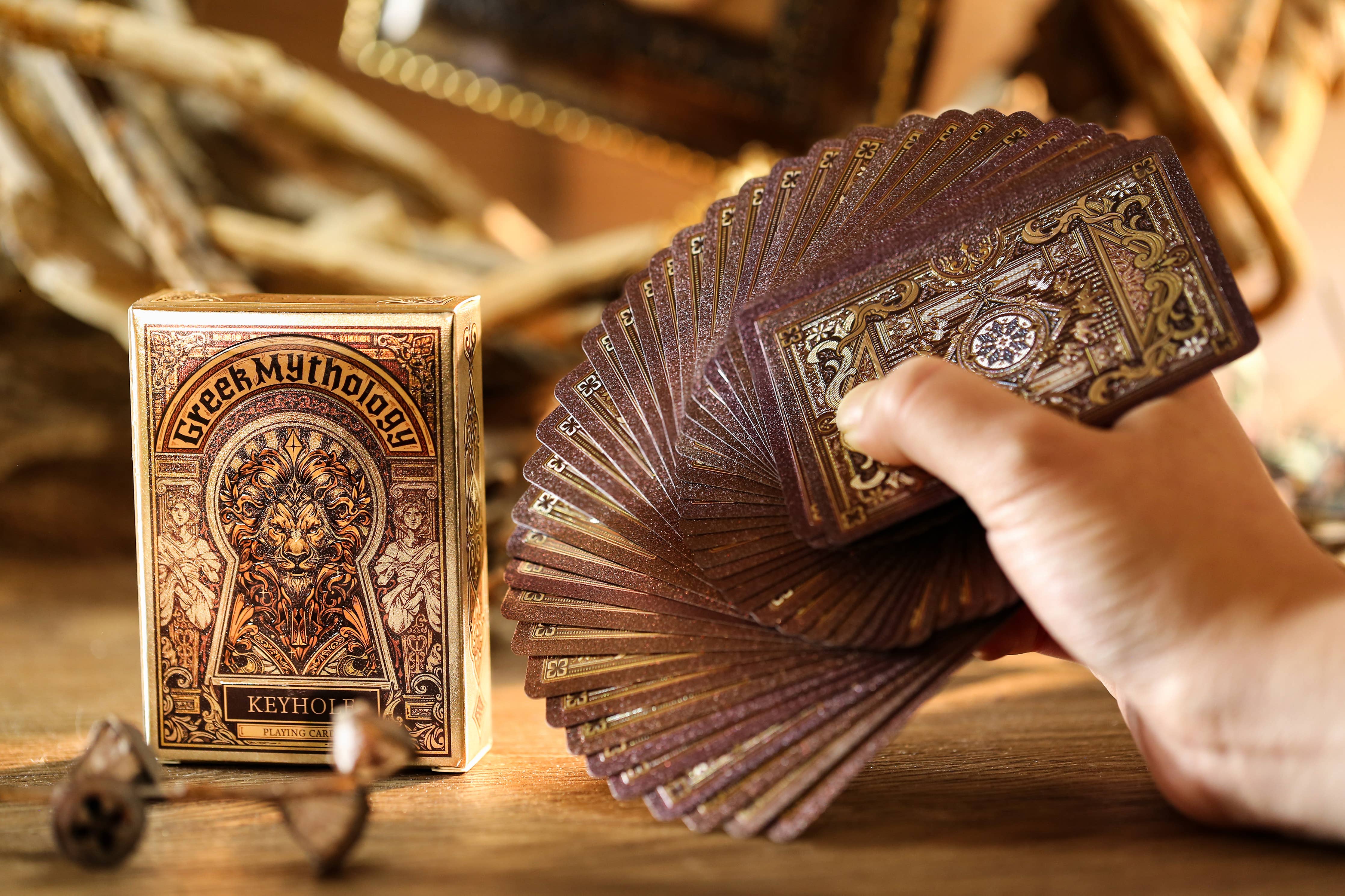 Hand holding a deck of Greek Mythology playing cards with the box in the background.