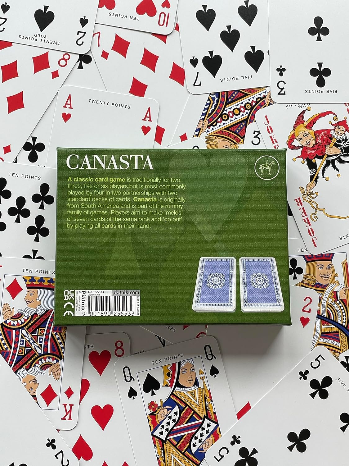 Canasta card game box surrounded by playing cards on a white background