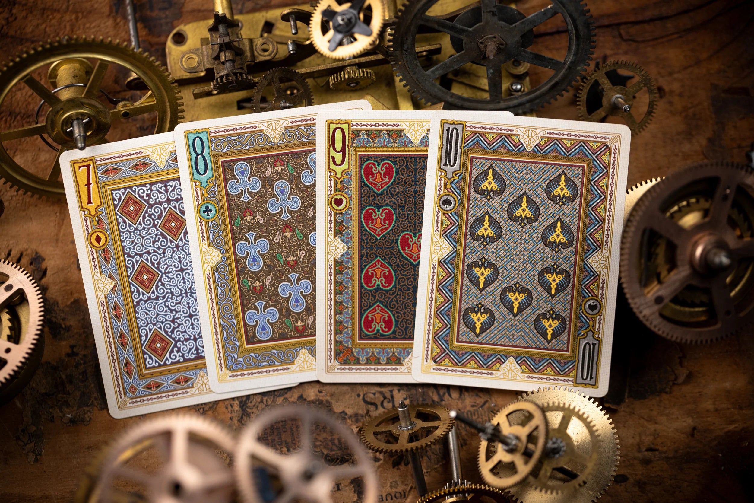 Four playing cards with intricate designs on a background of mechanical gears