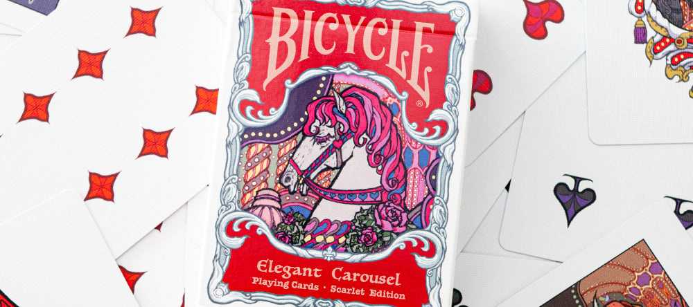 Bicycle Elegant Carousel Scarlet Edition tuck box centered on a background of custom playing cards