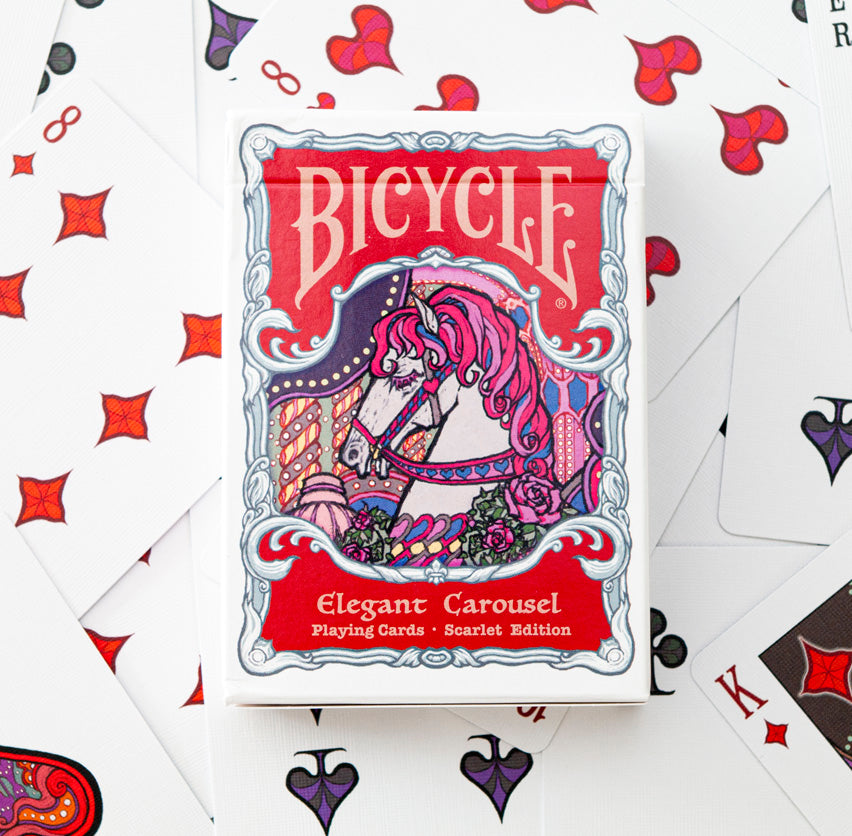 Bicycle Elegant Carousel Scarlet Edition tuck box displayed on top of spread playing cards