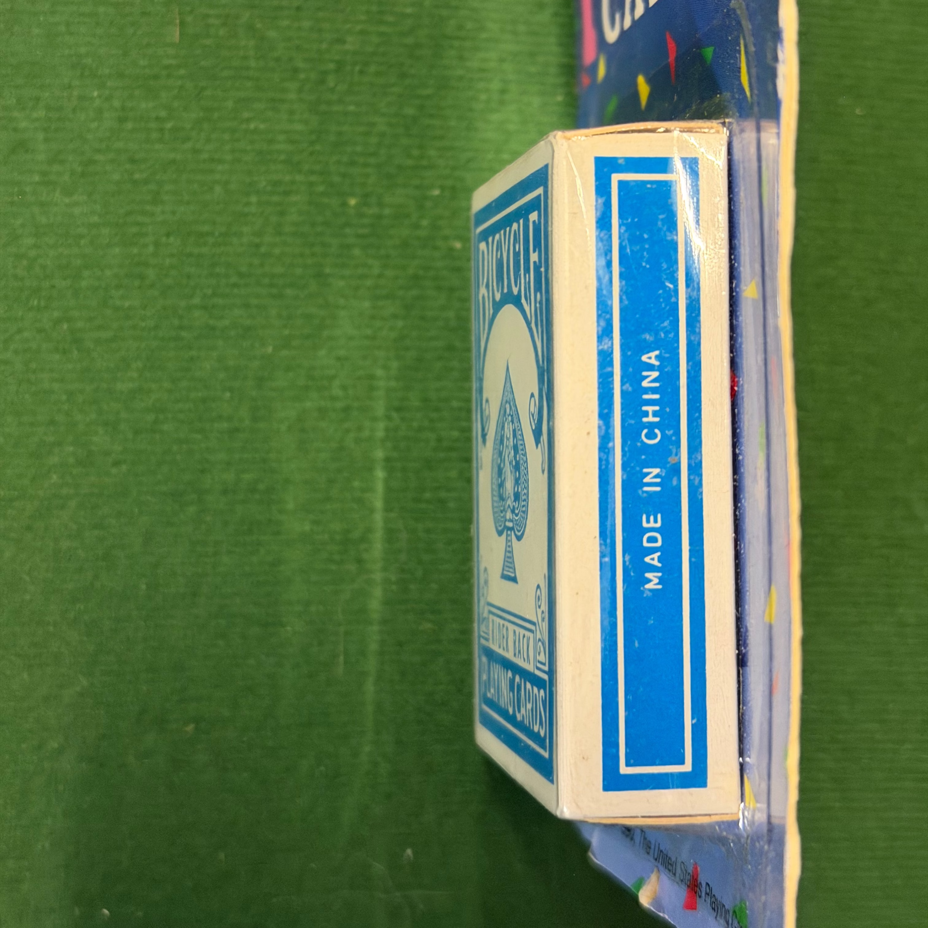 A deck of Bicycle playing cards in its original blue and white packaging, held vertically against a green felt surface.