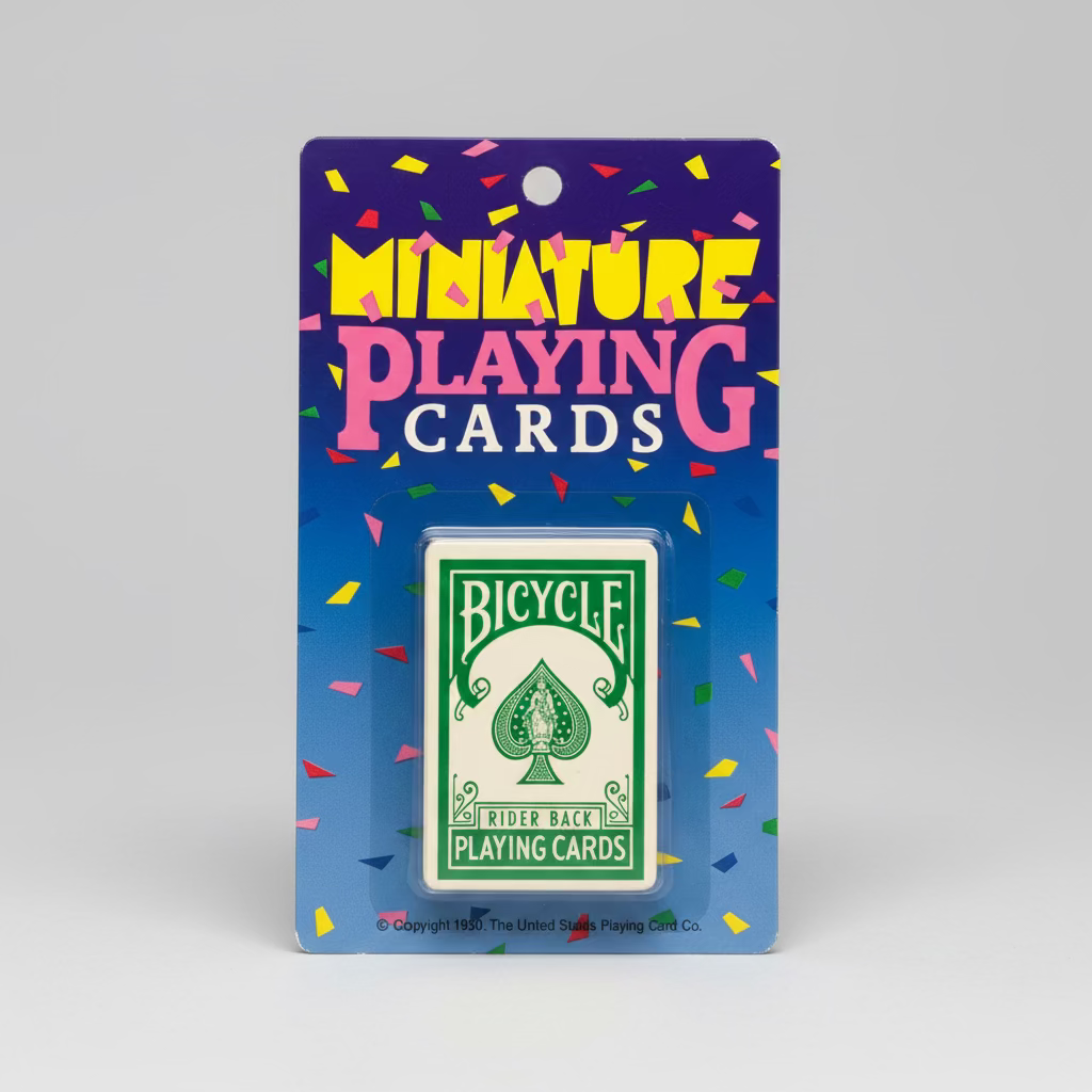 Bicycle miniature playing cards in a blue blister pack on a green felt-like surface. The package header reads 'MINIATURE PLAYING CARDS' with confetti graphics, and the card box inside shows the classic green Bicycle Rider Back design.