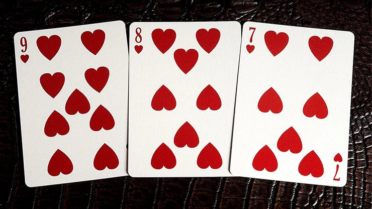 Three playing cards with red hearts on a dark surface