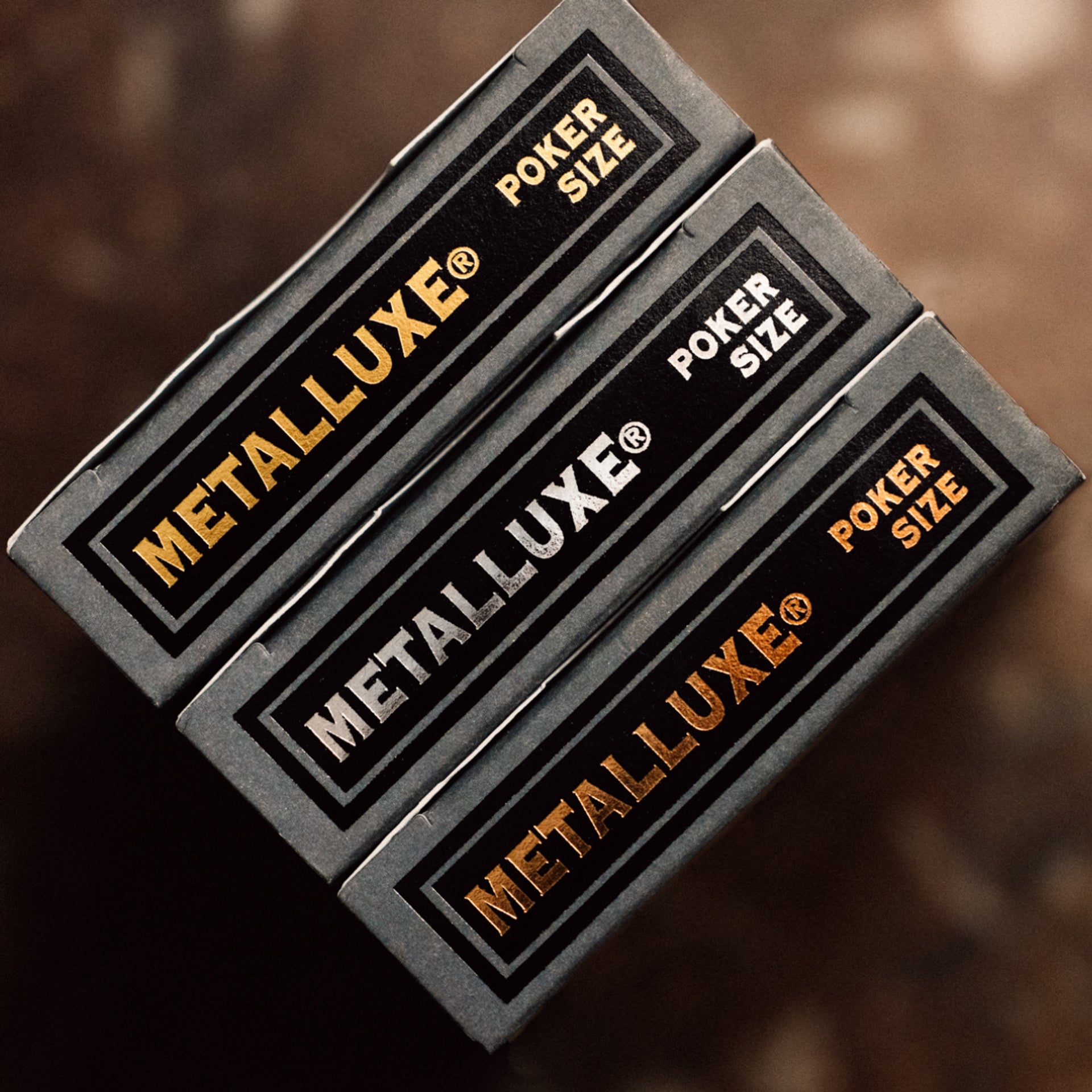 Three Black Metalluxe poker size card decks stacked on a dark background