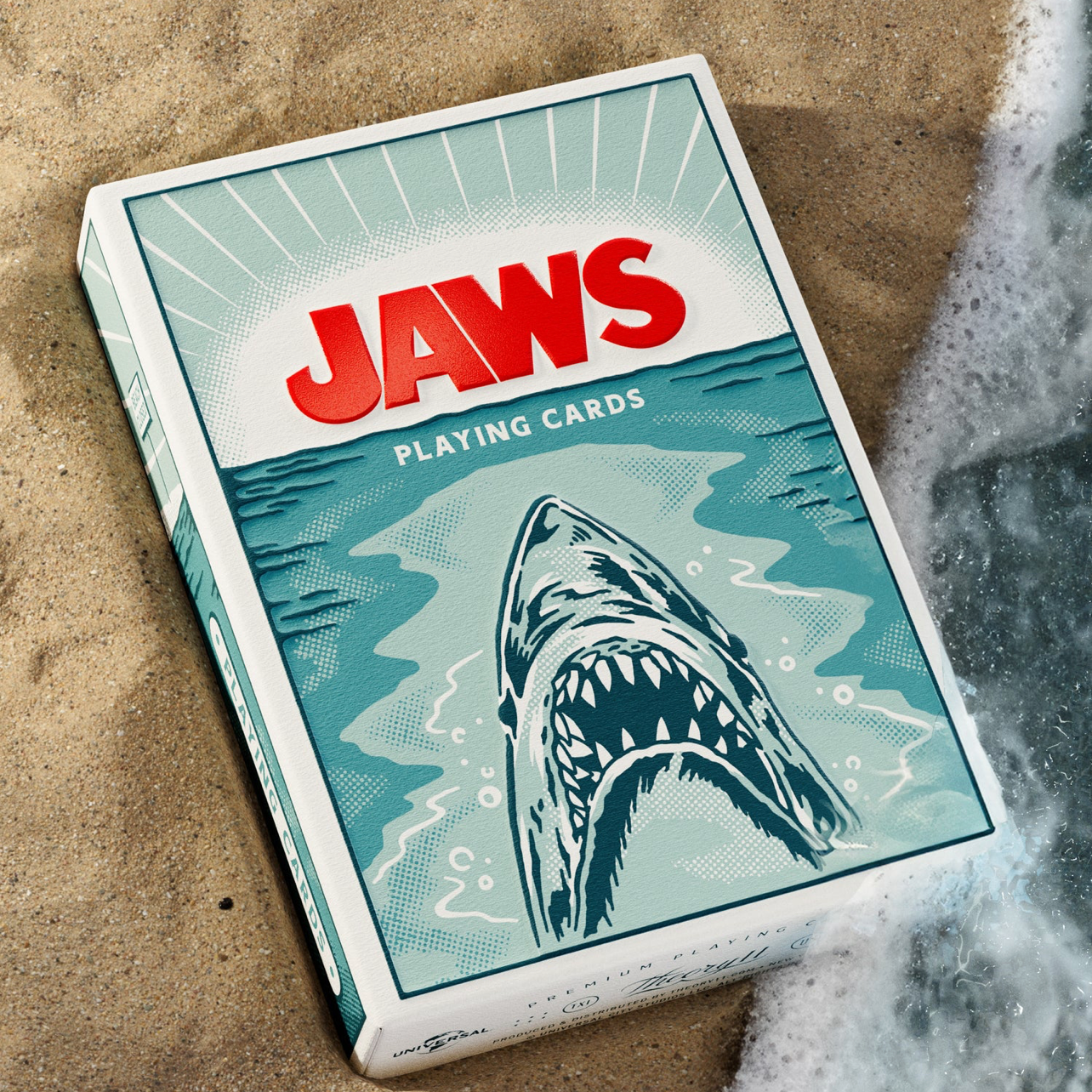 Theory11 JAWS Playing Cards tuck box on sand beside ocean foam