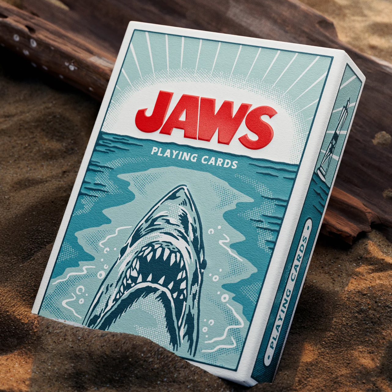 Theory11 JAWS Playing Cards box standing on beach sand with shark artwork