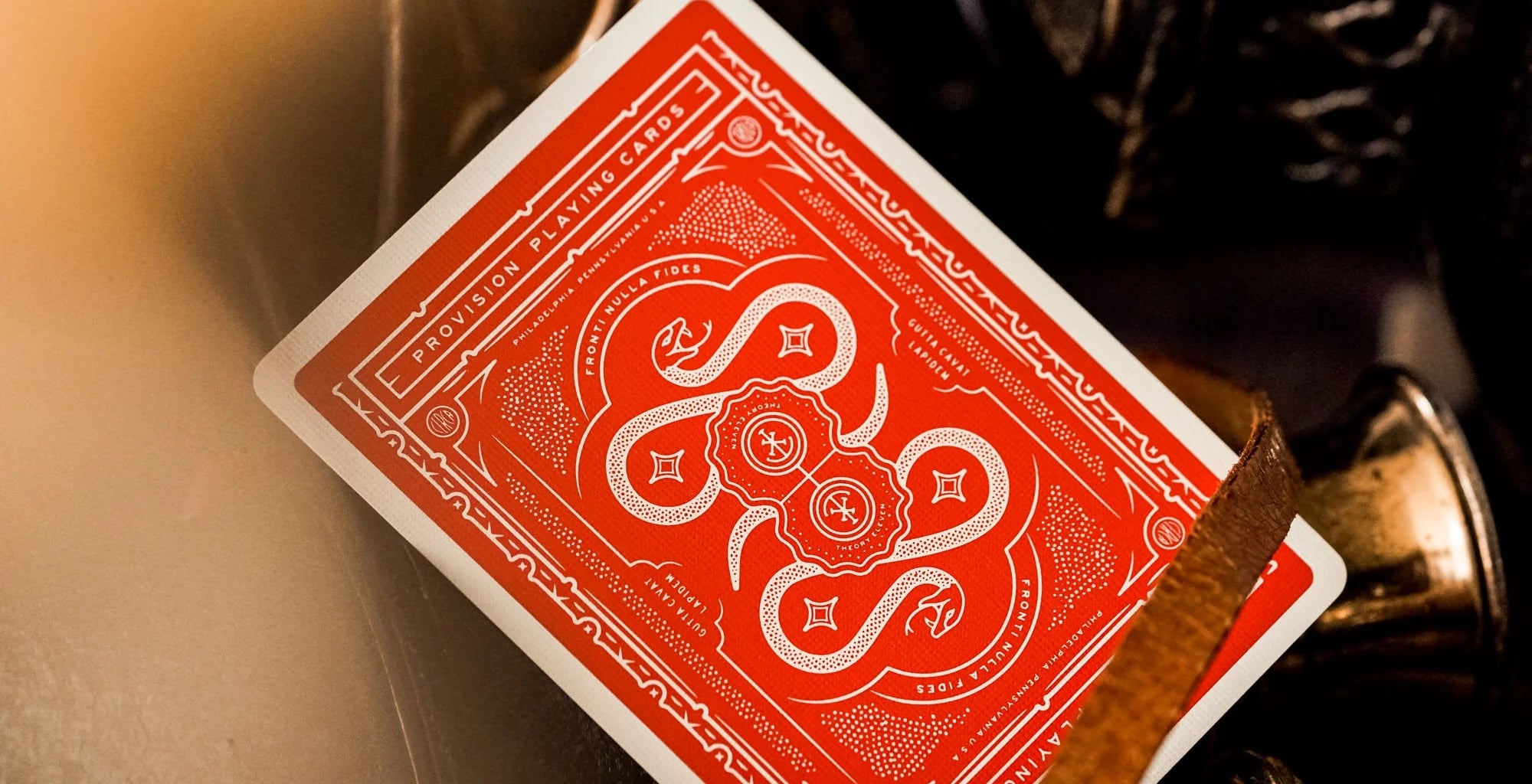 Red playing card with white design held by a metallic tool against a blurred background