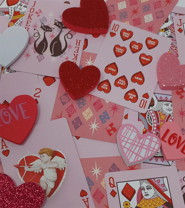 Valentine's Day-themed playing cards with hearts and decorative elements on a pink background.