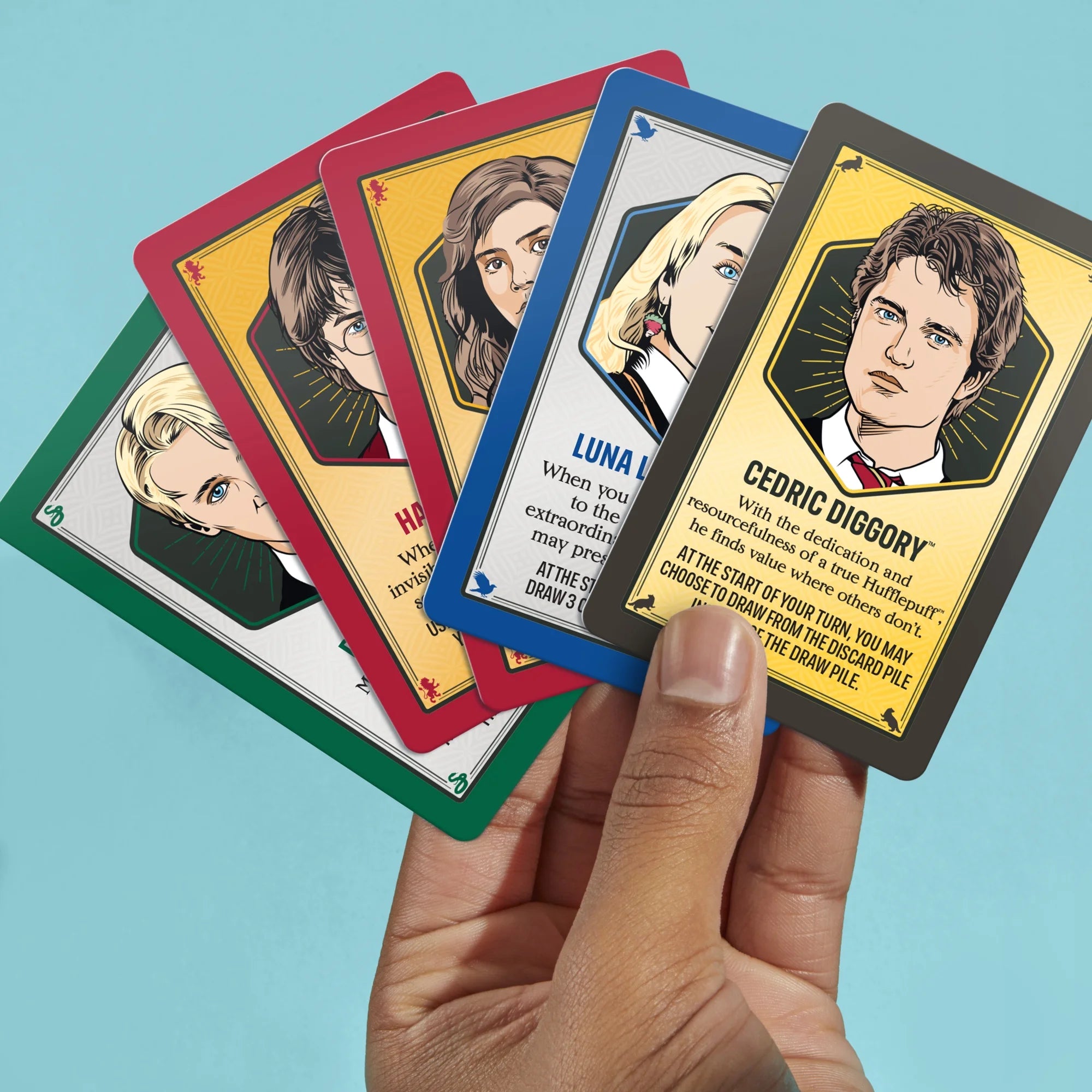 Hand holding a set of Monopoly Deal Harry Potter character trading cards with colorful borders against a blue background