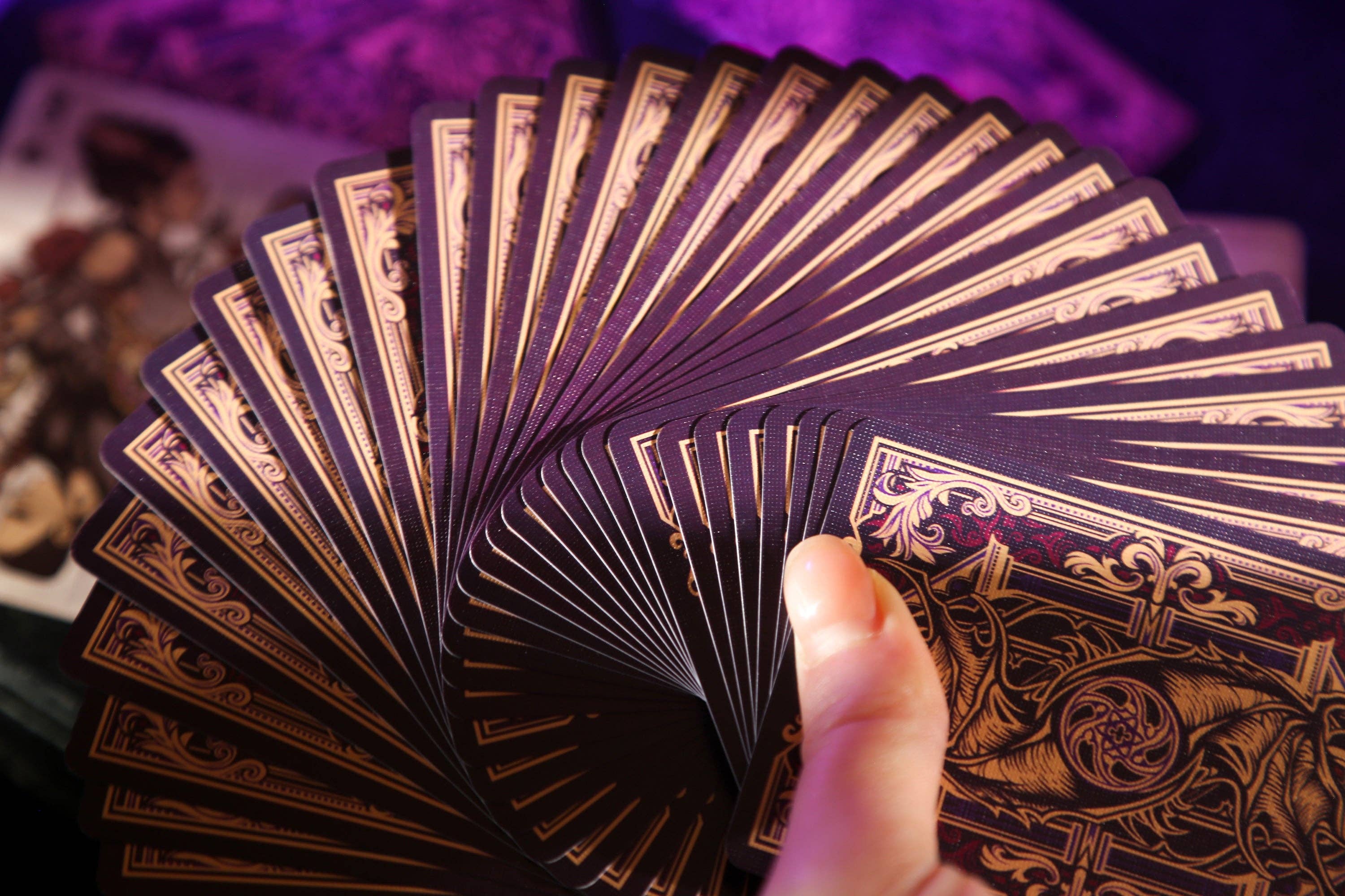Fanned-out deck of purple playing cards with gold text and designs.