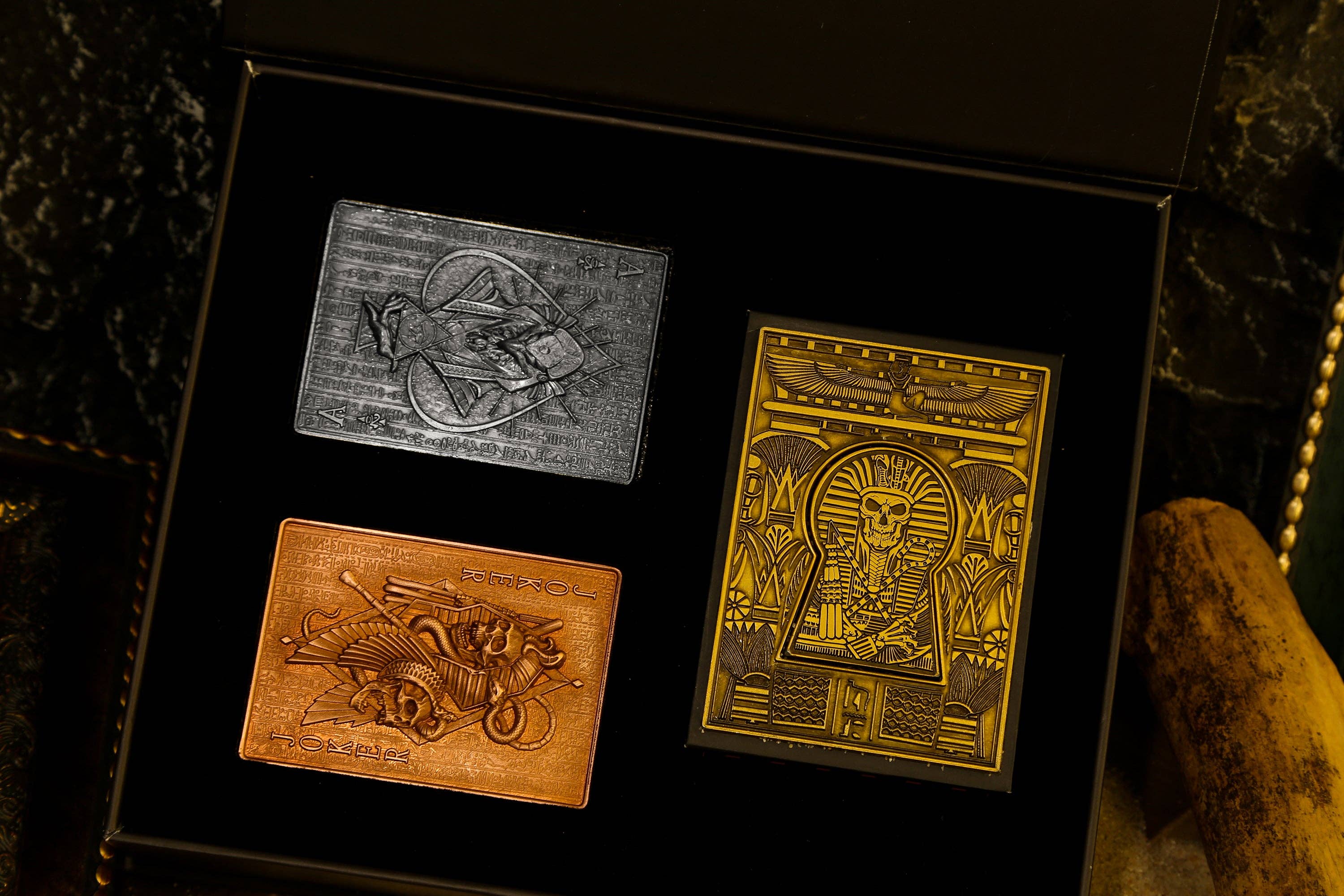 Three metallic collectible cards in a black display box on a dark stone surface.