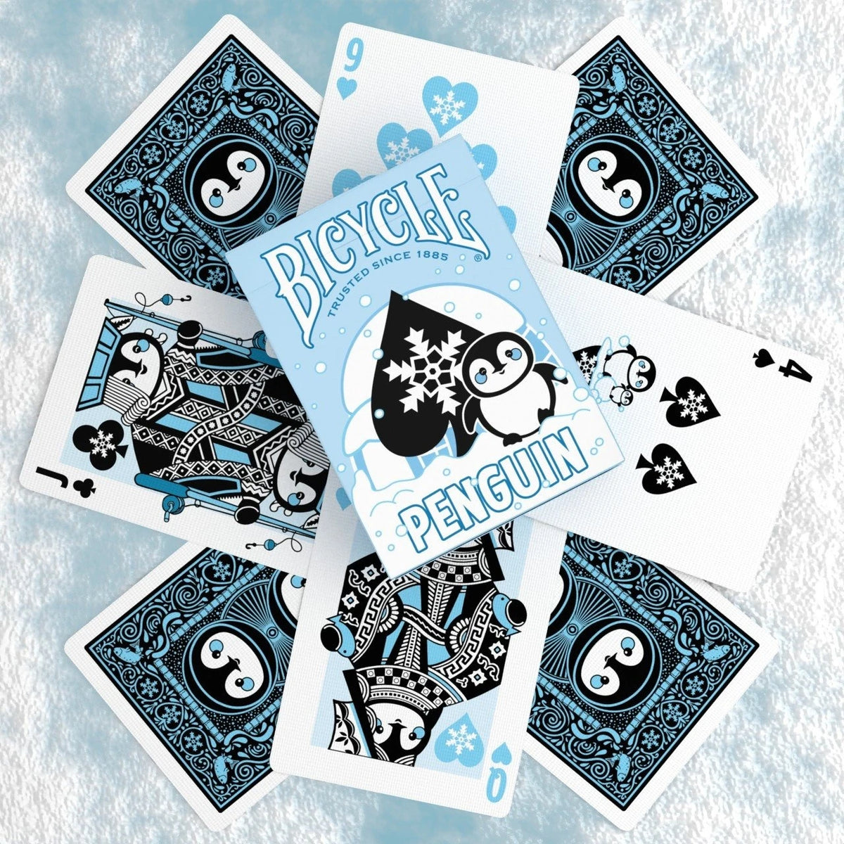 Bicycle Penguin tuck box centered over penguin card backs, a Jack, a Queen, and snowflake number cards on a snowy surface