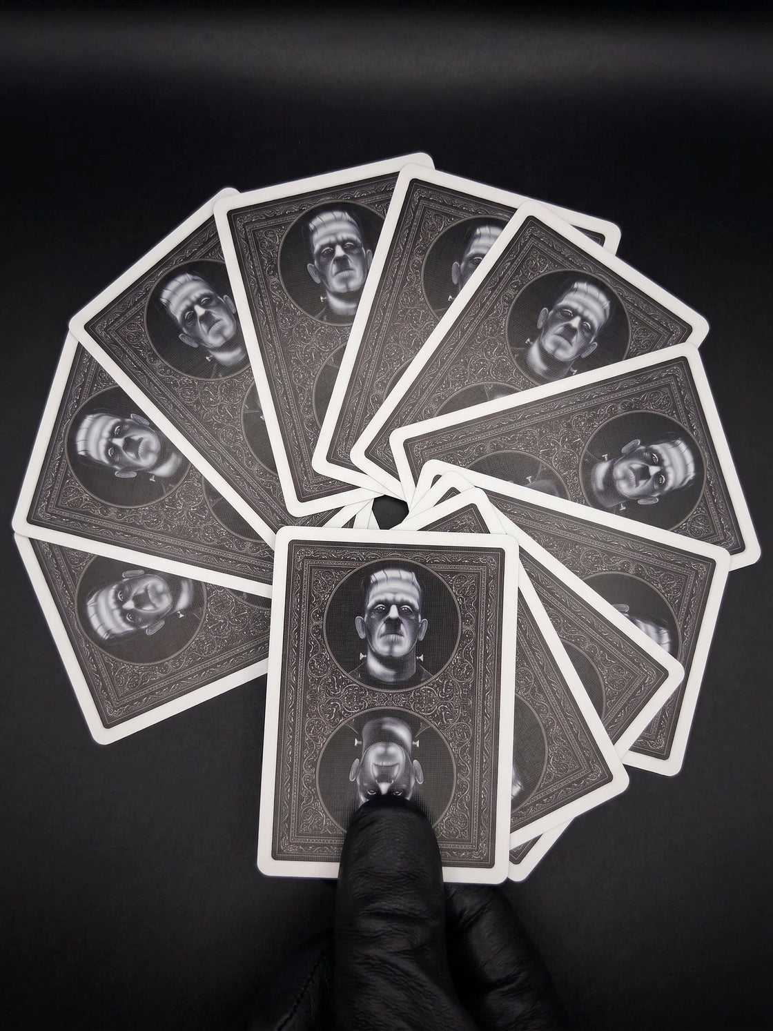 A gloved hand holding a circular fan of Classic Monsters card backs with mirrored Frankenstein portraits and white borders