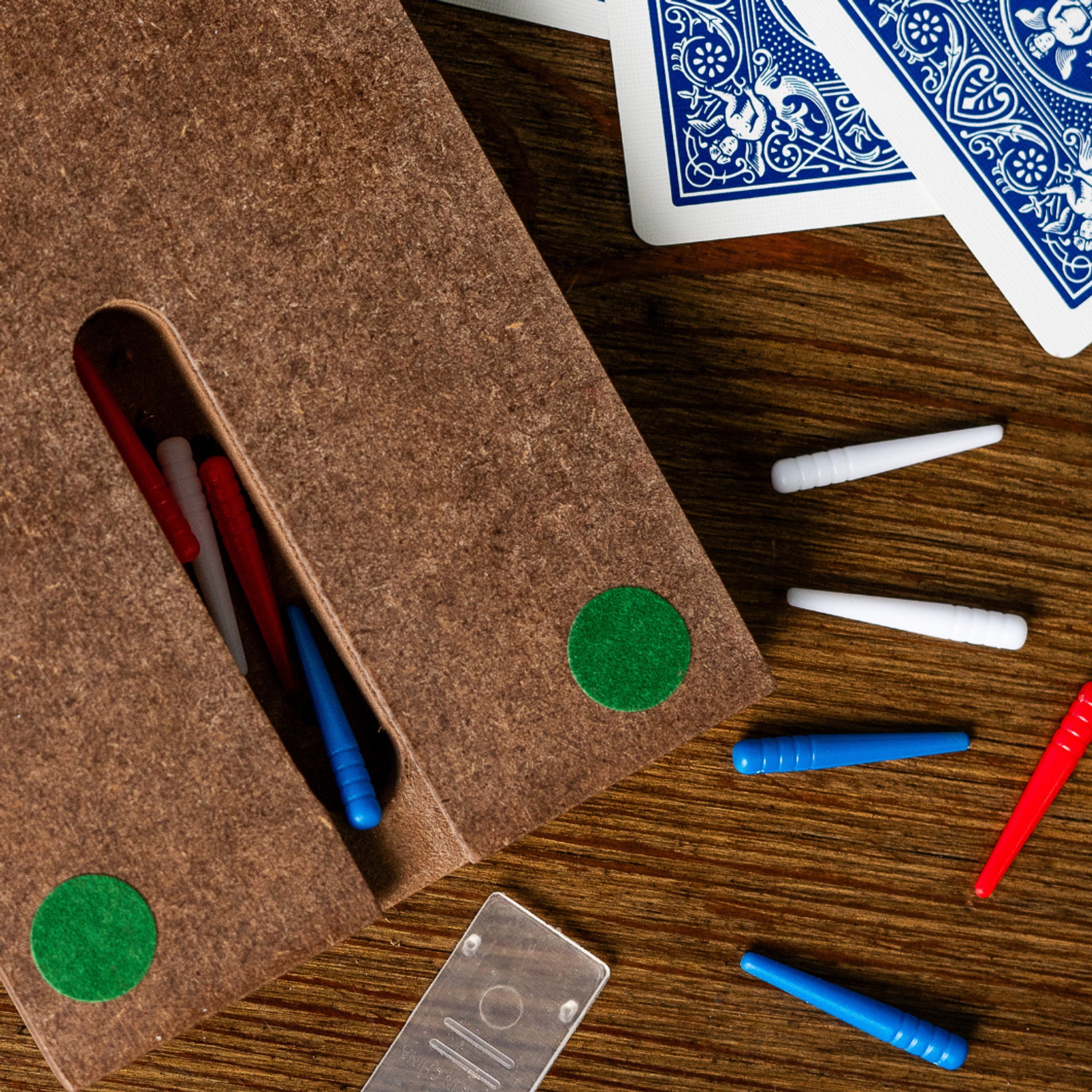 Brown felt pouch with green dots, pens, playing cards, and markers on a wooden surface.