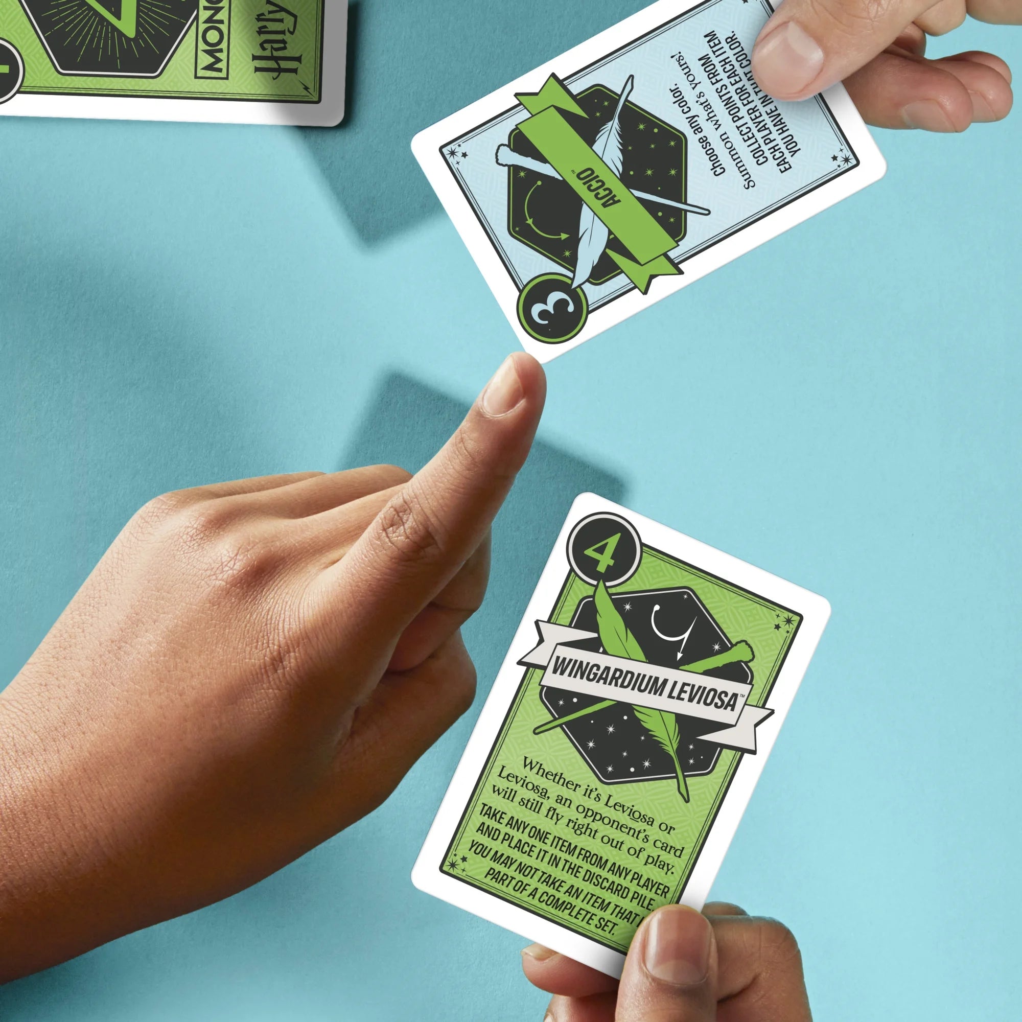Hands holding and comparing 'Wingardium Leviosa' and 'Accio' cards from a game on a blue background