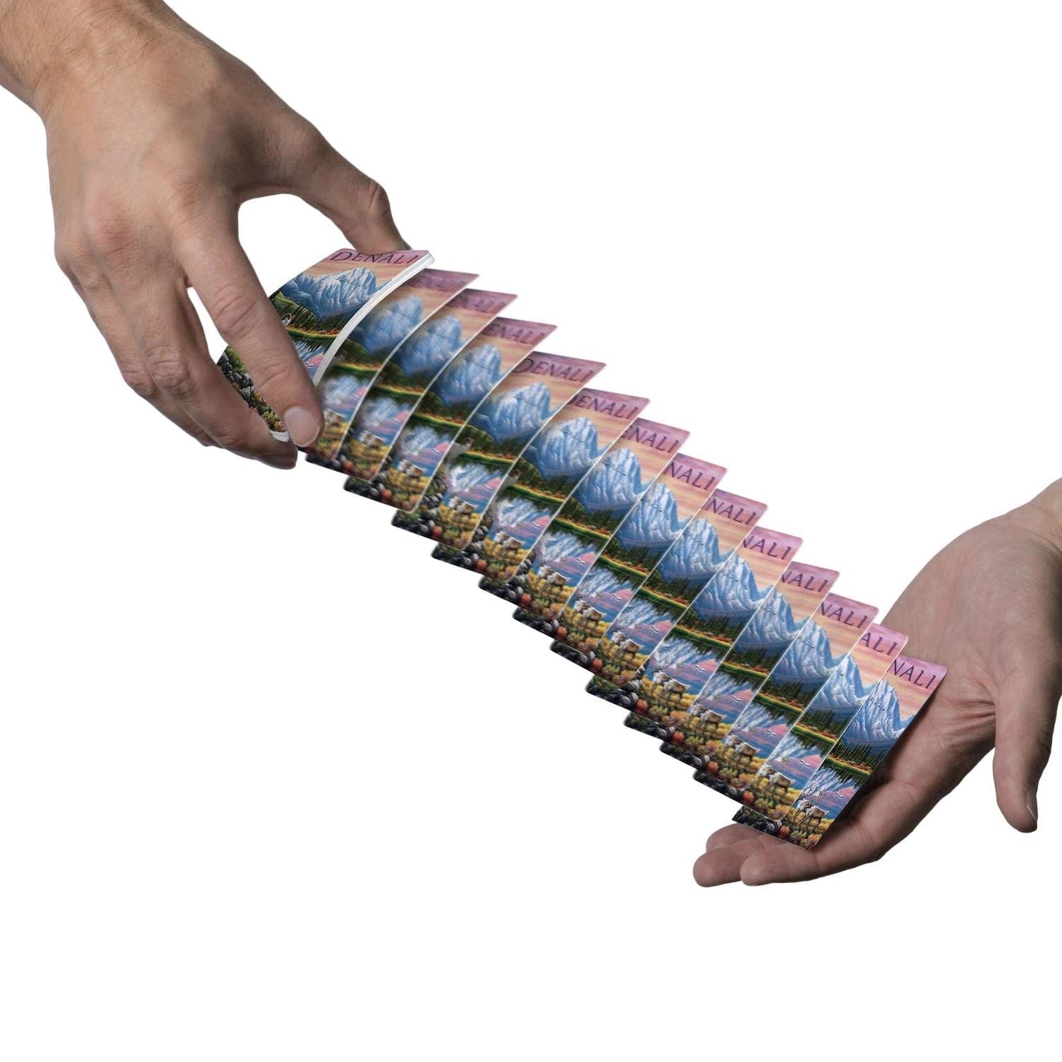 Denali playing cards cascading between two hands with Mount McKinley scenic backs visible