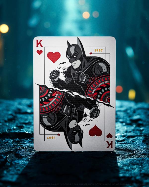 Playing card with Batman design on a dark, textured surface with blurred lights in the background