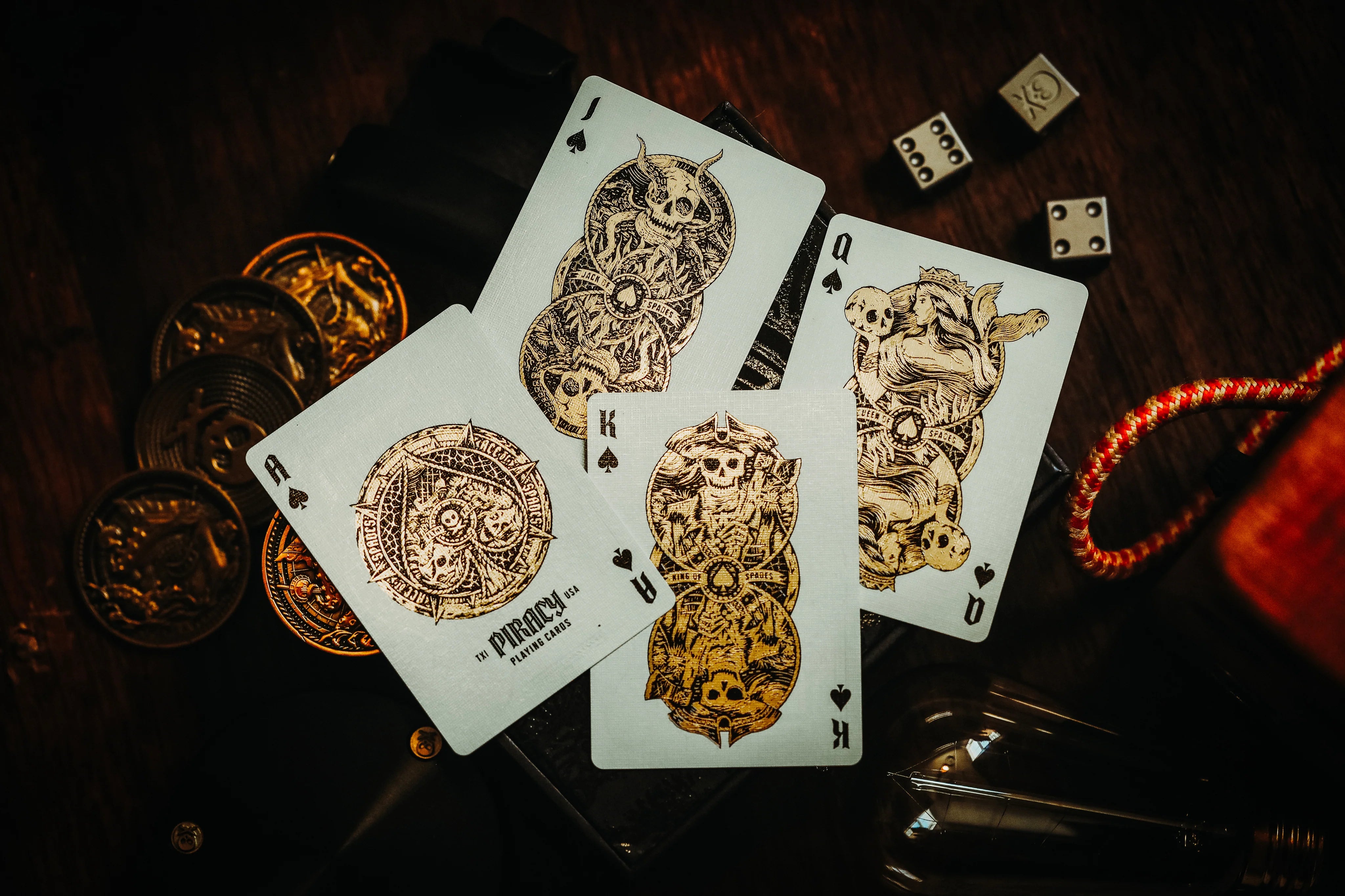 Decorative Piracy playing cards with gold designs on a dark surface with coins and dice.