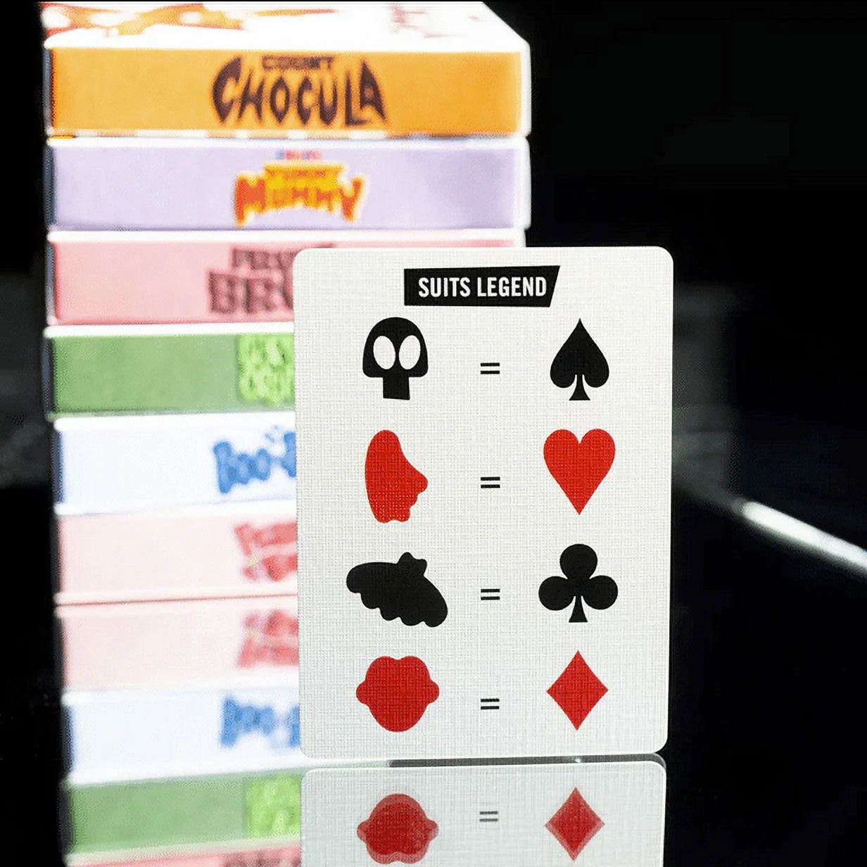 Franken Berry playing cards with suit symbols and a stack of colorful card boxes in the background.
