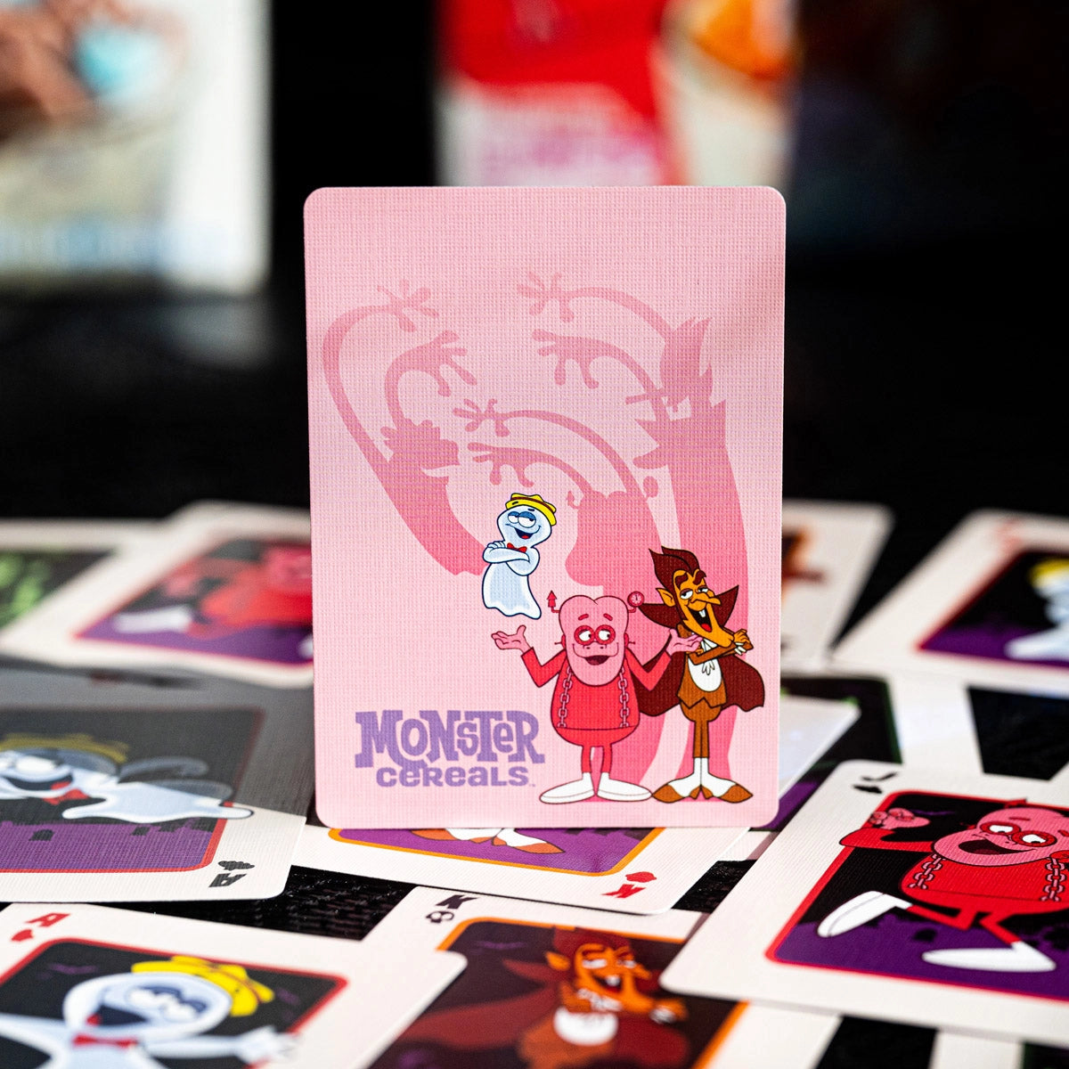 Pink Monster Cereals artwork card featuring Boo Berry, Franken Berry, and Count Chocula above scattered card faces.