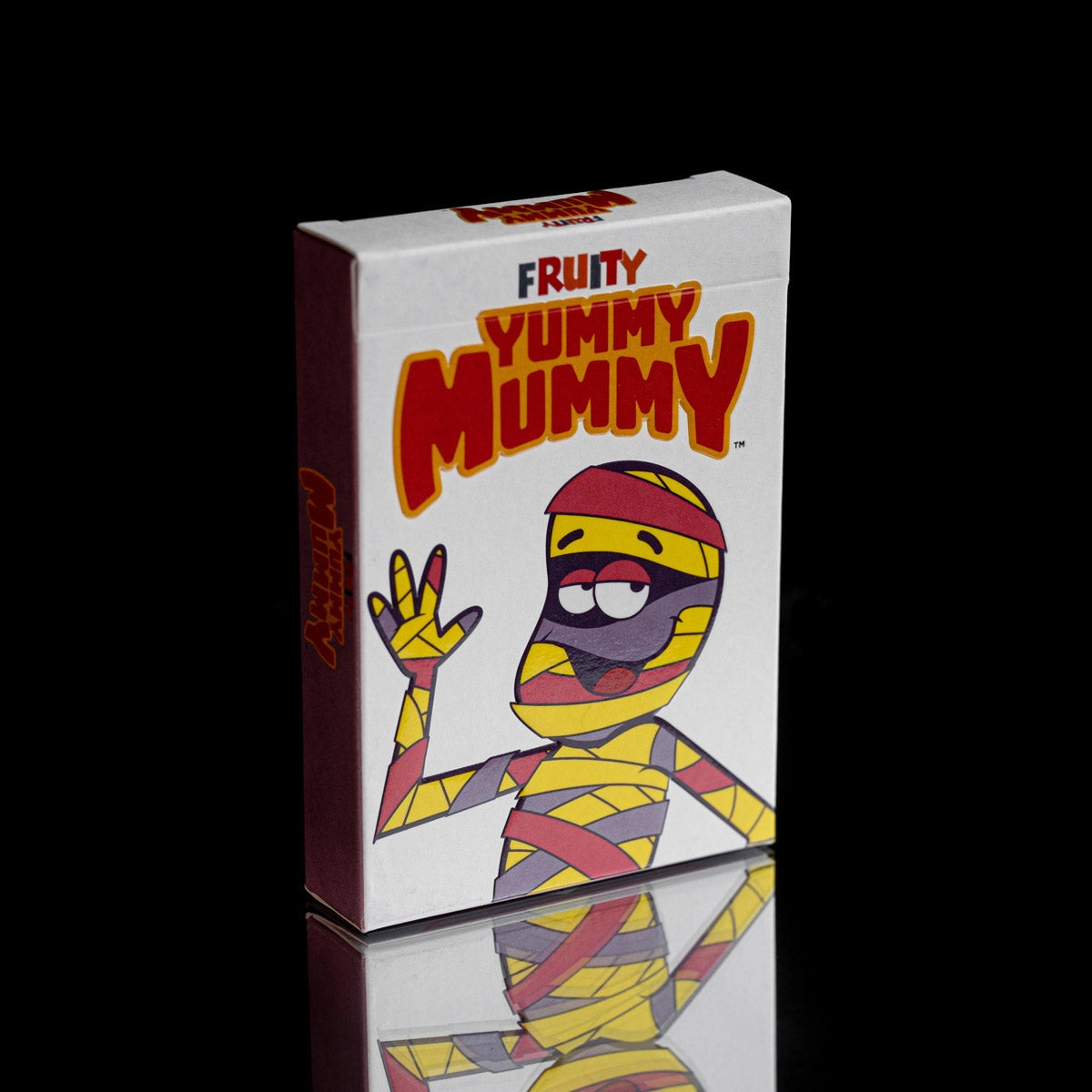 Angled front and side view of the Fruity Yummy Mummy playing cards tuck box on a reflective black surface.