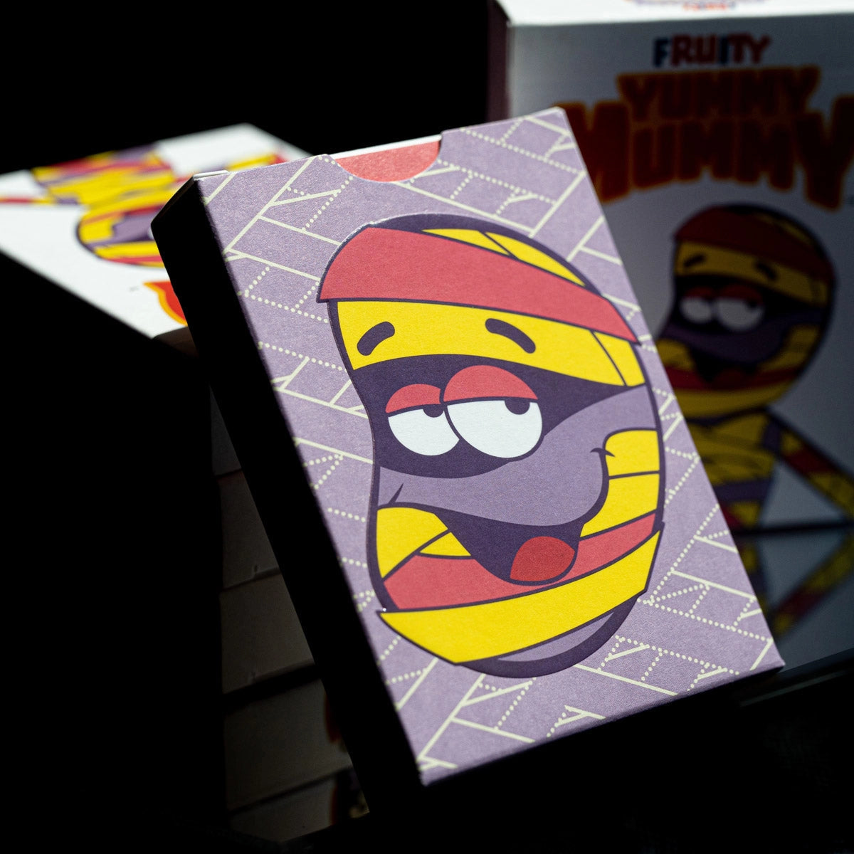 Back of the Fruity Yummy Mummy tuck box with a large character portrait and purple bandage-pattern artwork.