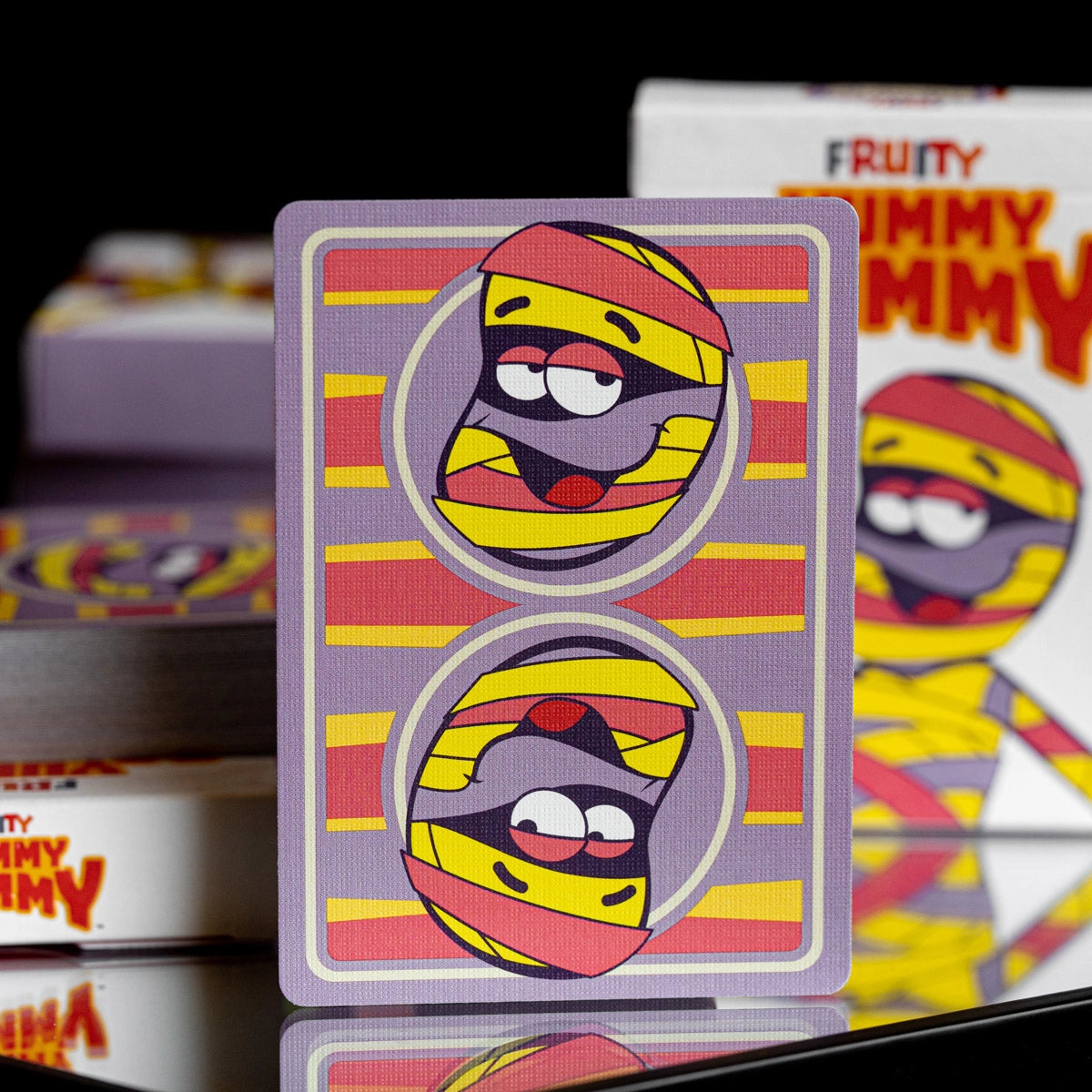 Fruity Yummy Mummy card back with mirrored character portraits and purple, yellow, and red stripes.