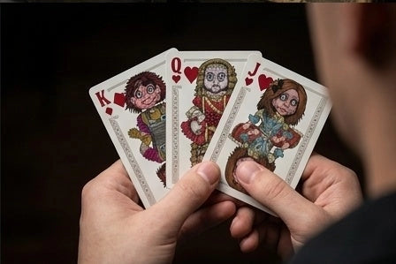 Hands holding Haunted Dolls Playing Cards with an illustrated King of diamonds, Queen of hearts, and Jack of hearts