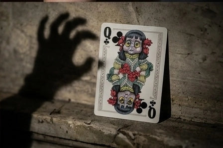 Haunted Dolls Playing Cards Queen of clubs propped on a stone ledge beside the shadow of an outstretched hand