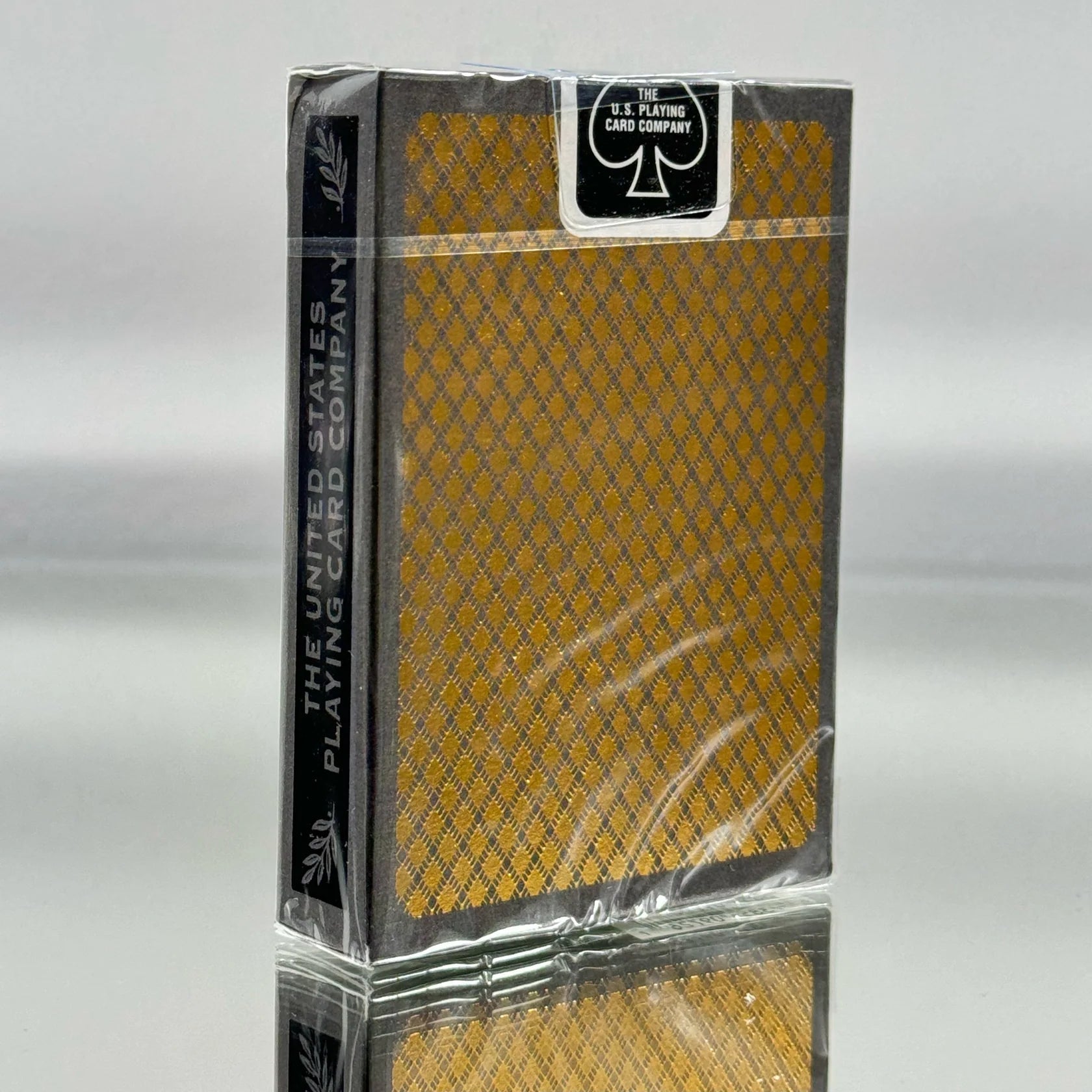 Deck of Bee metalluxe playing cards with a gold and black design on a gray background