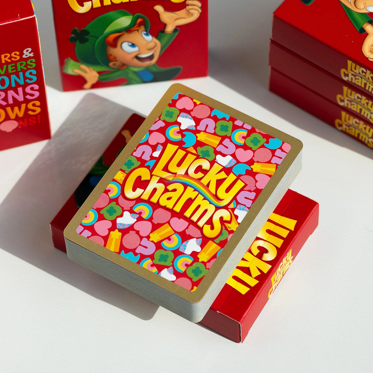Lucky Charms deck resting diagonally on a red tuck box with its gold-bordered marshmallow card back visible.