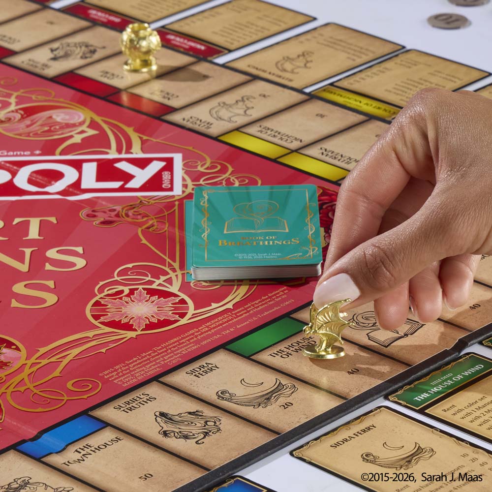 A player moves a golden token beside the themed cards on the Monopoly A Court of Thorns and Roses board.