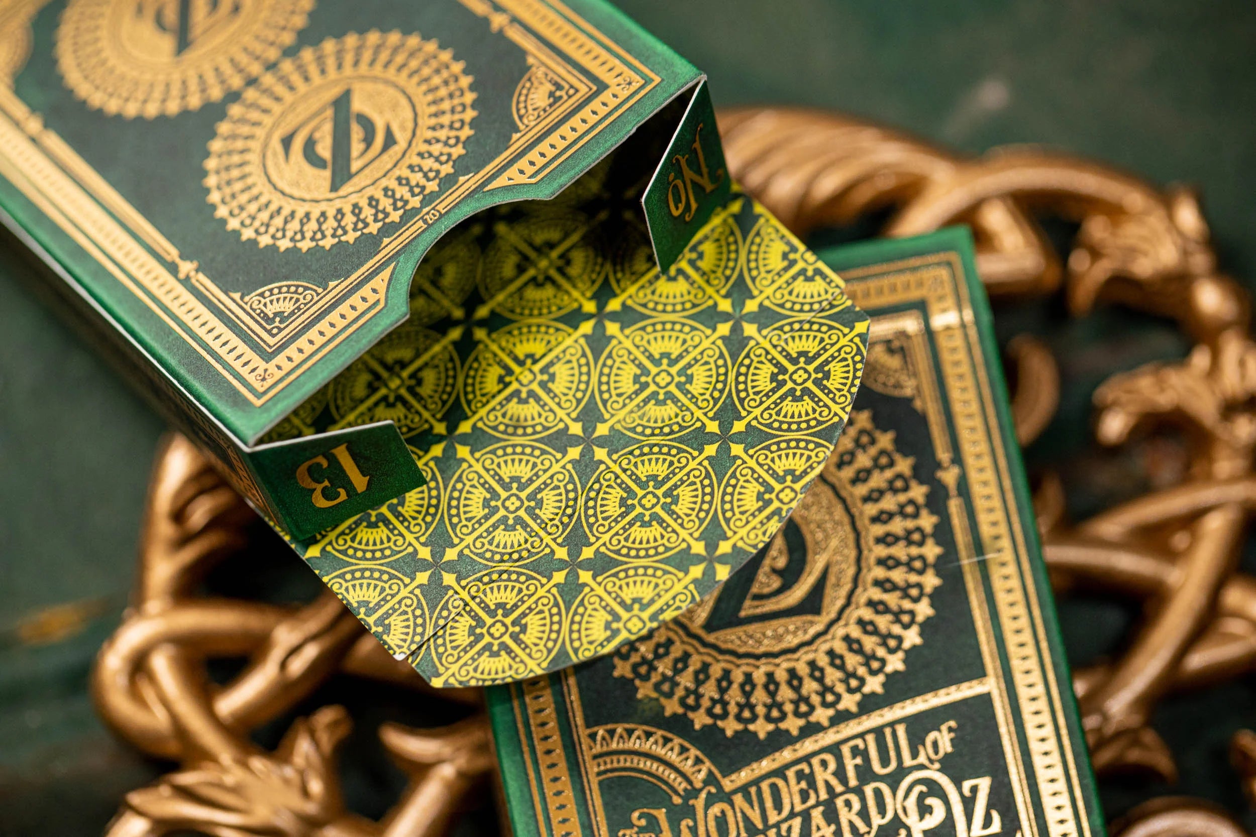 Green and gold playing card box with intricate designs on a dark background