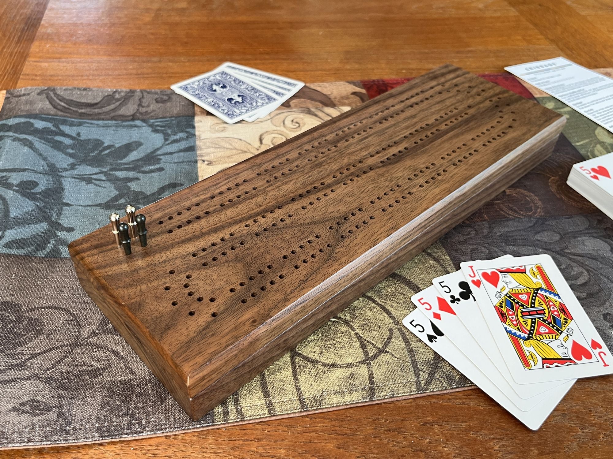 Wooden cribbage board with playing cards on a patterned tablecloth