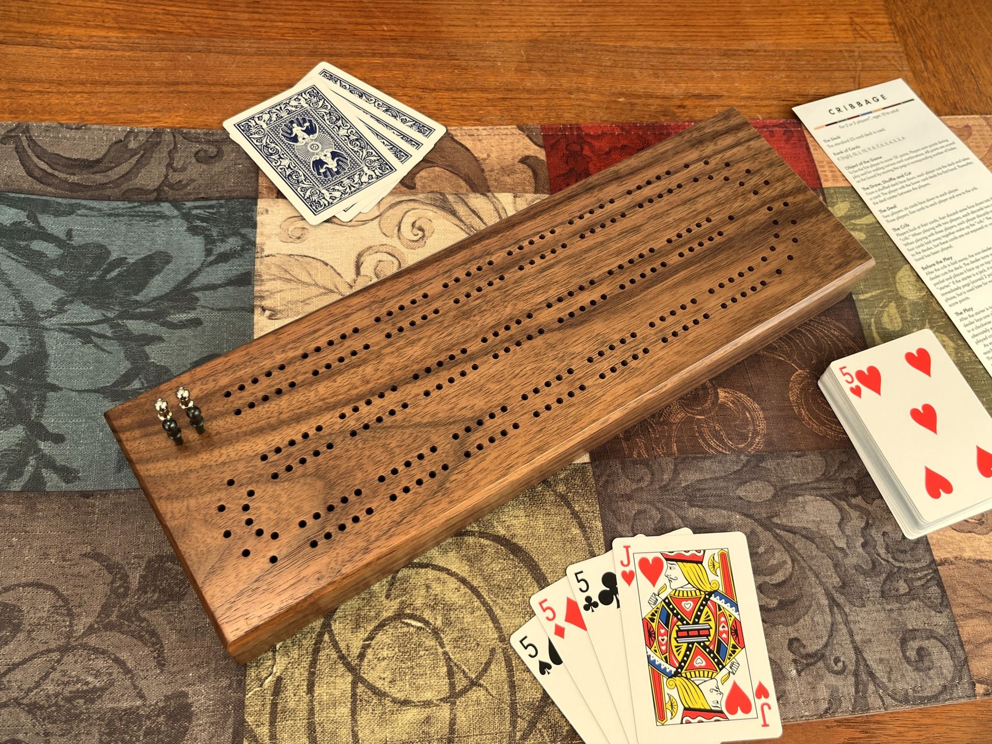 Wooden cribbage board with playing cards on a patterned surface