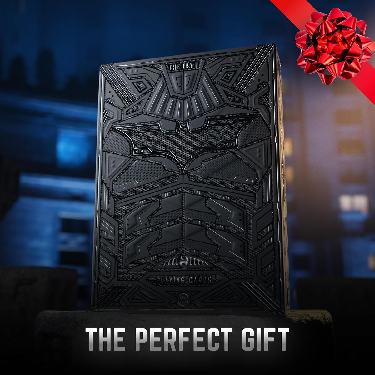 Theory11 The Dark Knight tuck box against a nighttime city backdrop, with a red gift bow graphic and The Perfect Gift caption.