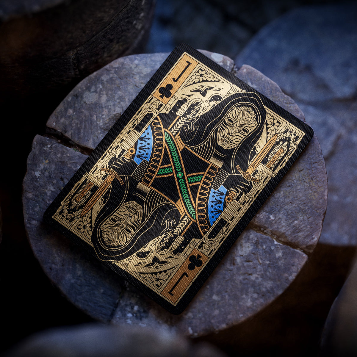 Theory11 Kovadrin Jack of Clubs with mirrored gold, blue, and green court artwork displayed on a round stone pedestal.