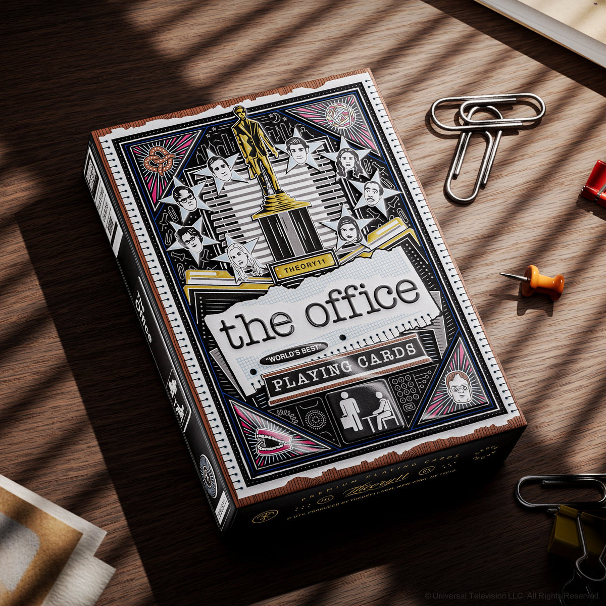 Angled front view of The Office Playing Cards tuck box beside paper clips on a desk