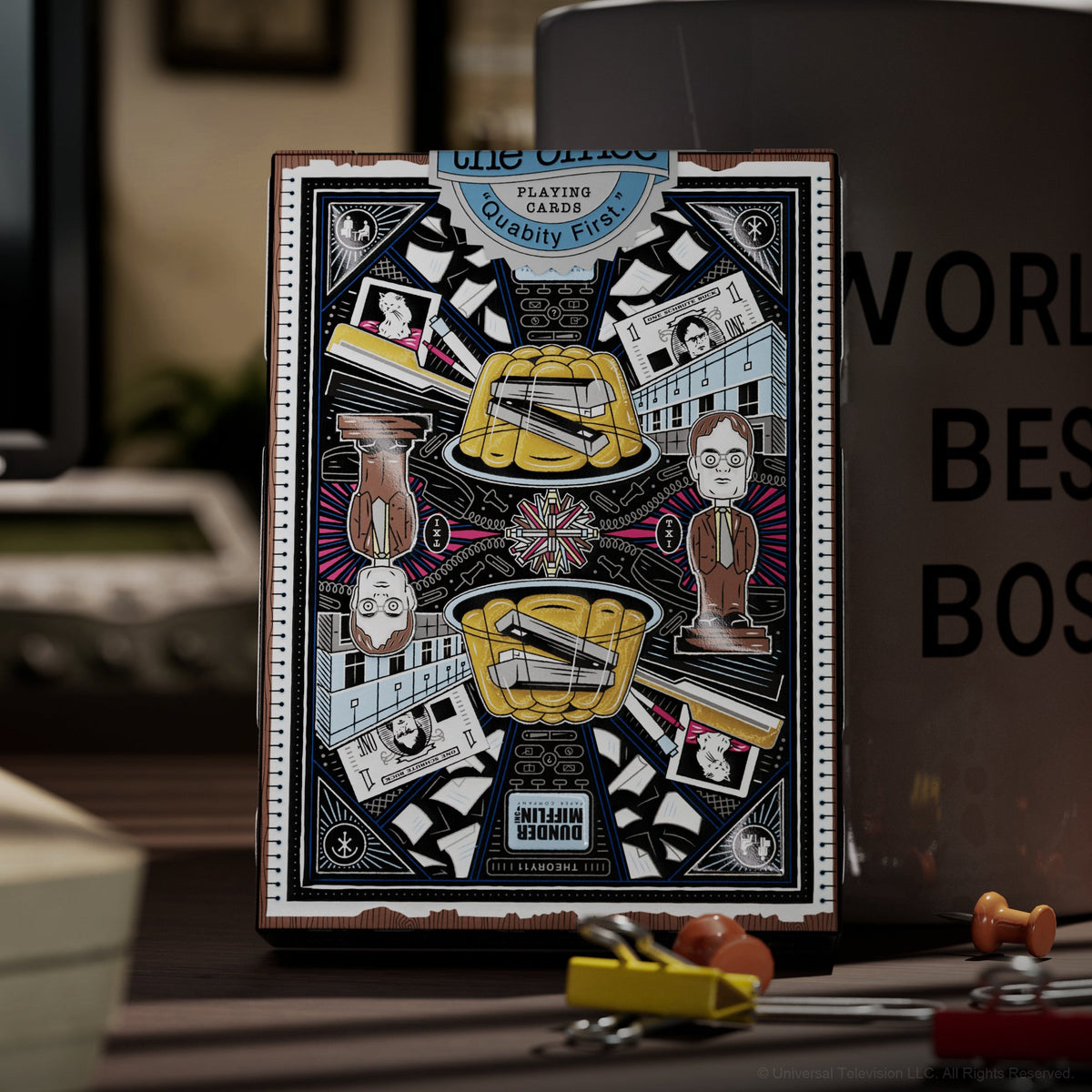 Rear artwork of The Office Playing Cards tuck box displayed in front of a World's Best Boss mug