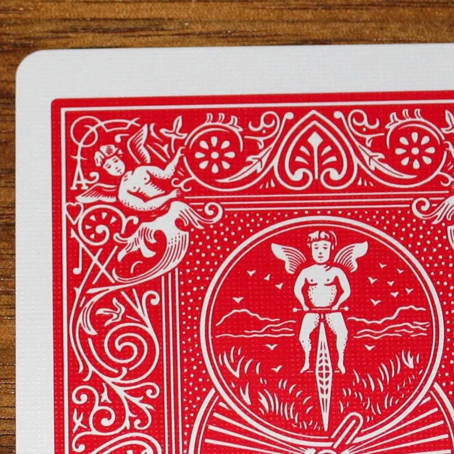 Close-up of a red Bicycle Ultimate Marked deck playing card with white designs on a wooden surface