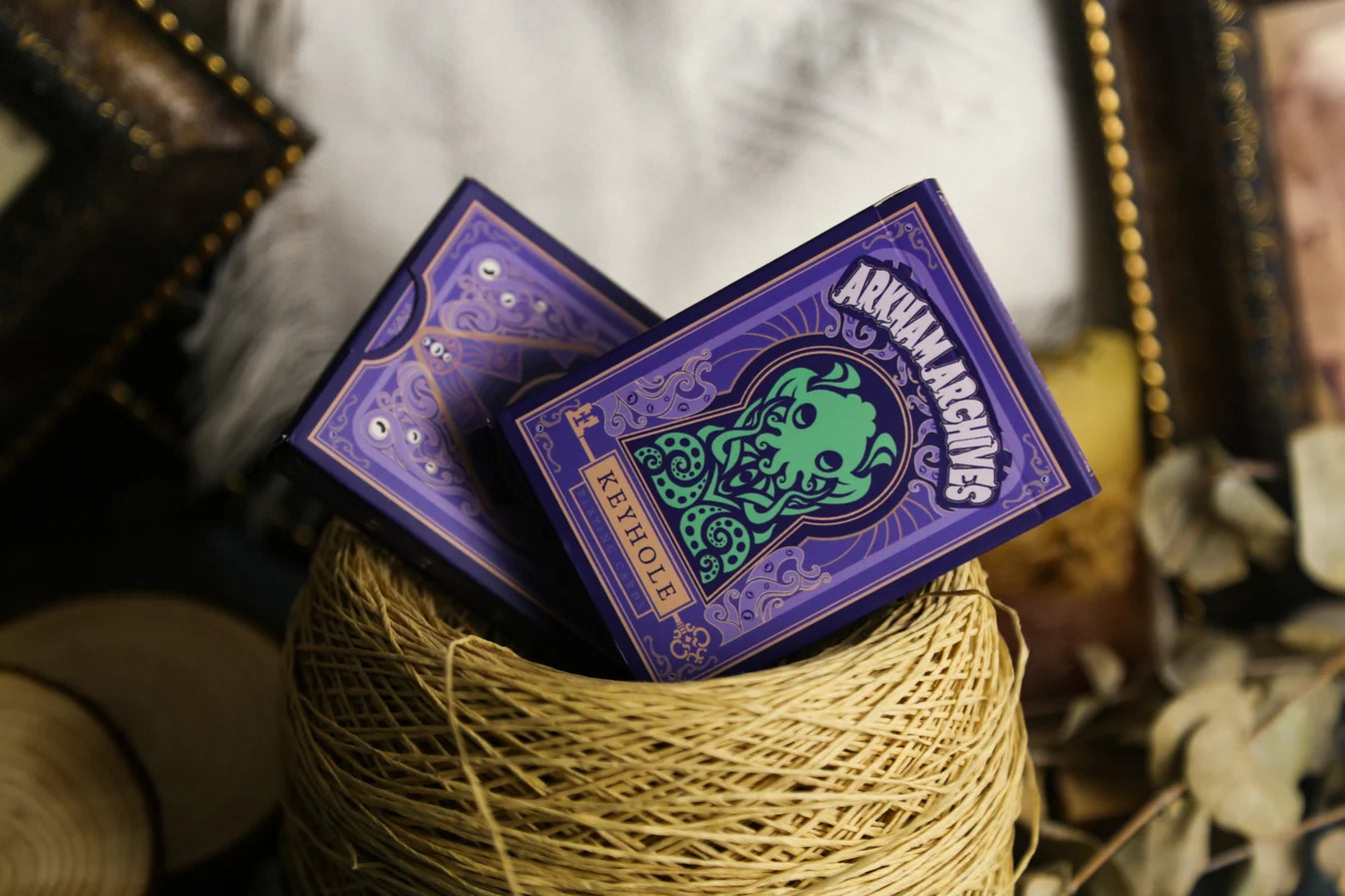 Arkham Archives purple Keyhole playing card tuck boxes displayed in a woven basket